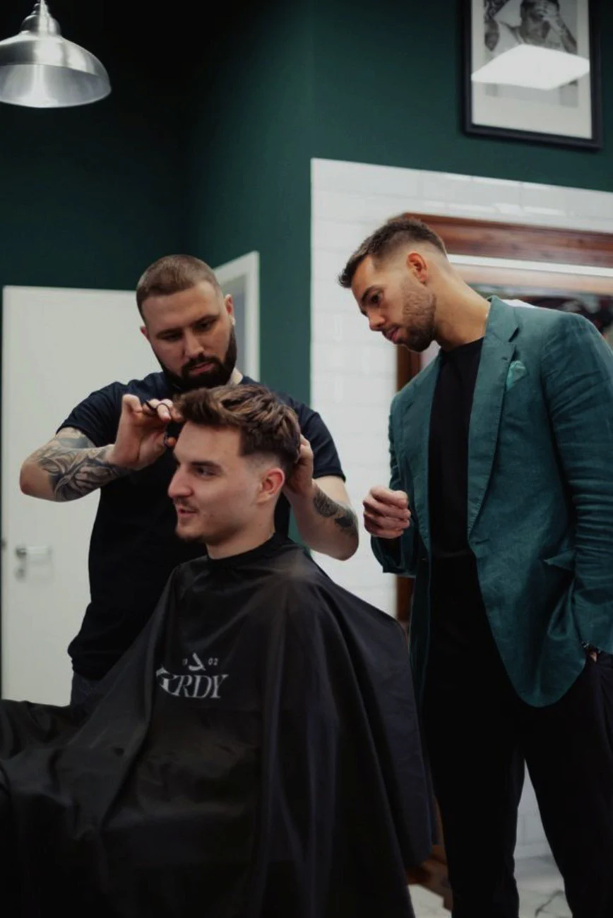 Barber in a green jacket cutting a client's hair at Koródy Barber Shop
